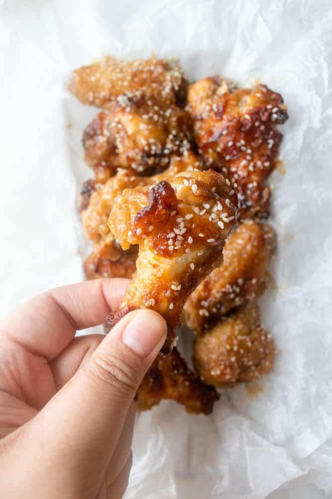 a hand is holding up a drummy of the Sesame Ginger Chicken Wings