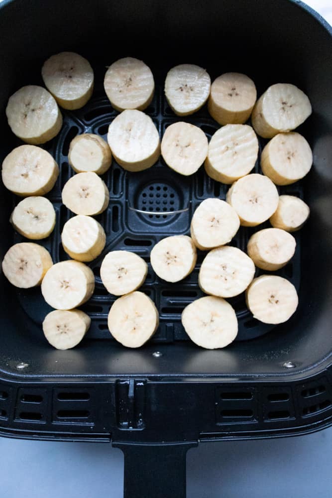 sliced green plantains in air fryer basket