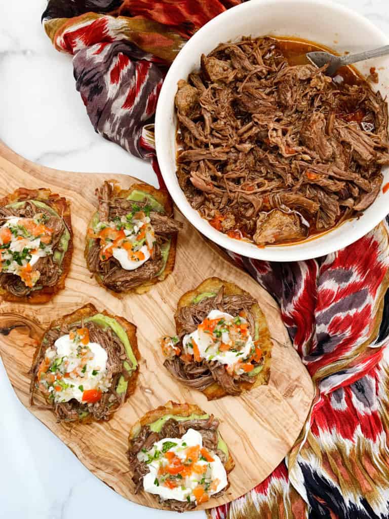 Spicy shredded beef tostadas on a wooden board and a bowl of spicy shredded beef