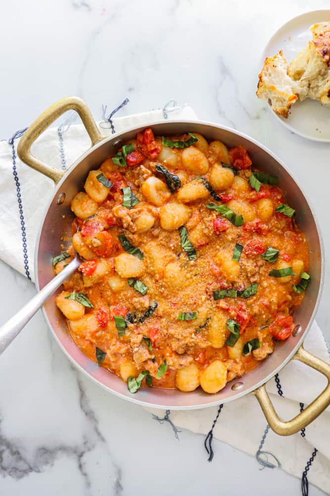 creamy spicy sausage gnocchi in a skillet with a serving spoon in it