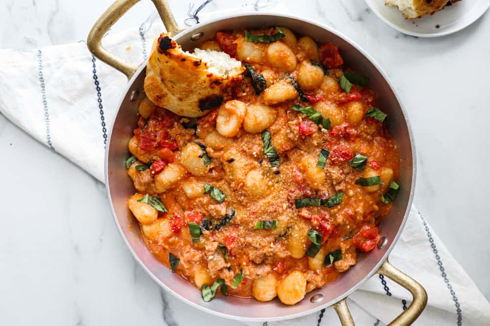 creamy spicy sausage gnocchi in a skillet with a crusty piece of bread dipped in the sauce