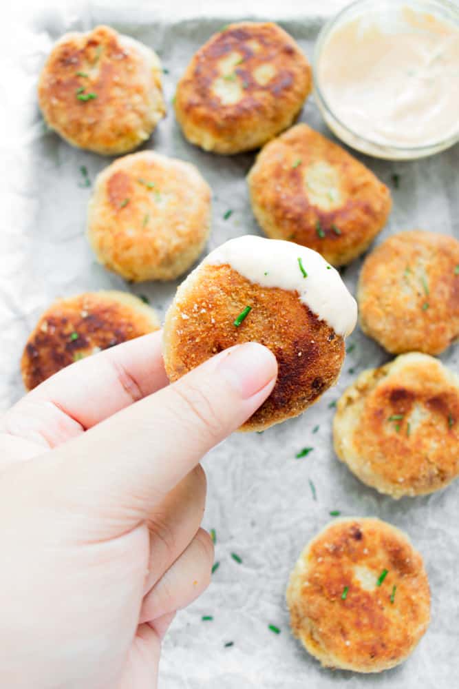 spicy chicken croquettes on a platter and one is being held and it's dipped in a sauce