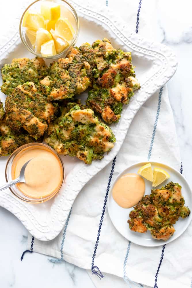 chicken broccoli fritters on a platter and one on a plate with dipping sauce and lemon wedges