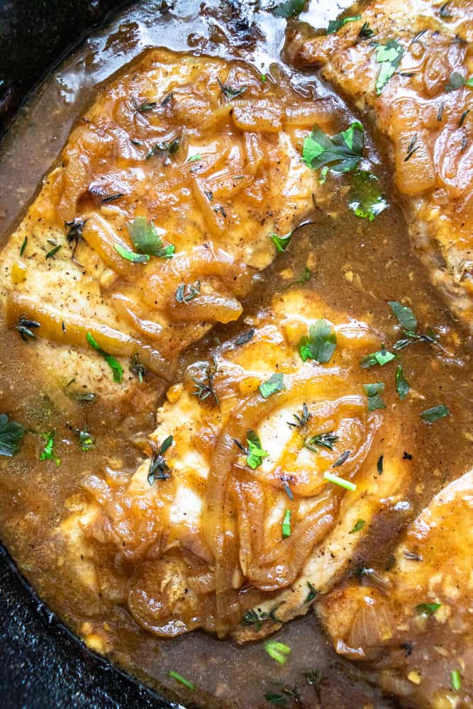 french onion smothered pork chops up close in a skillet