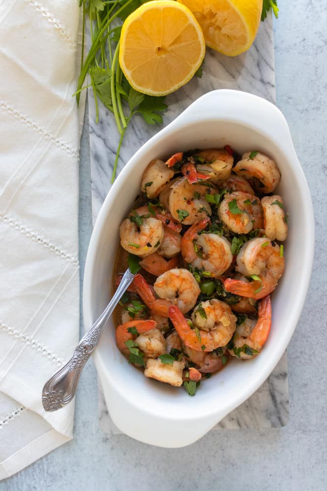 shrimp scampi in a dish with lemons and parsley above it on a tray