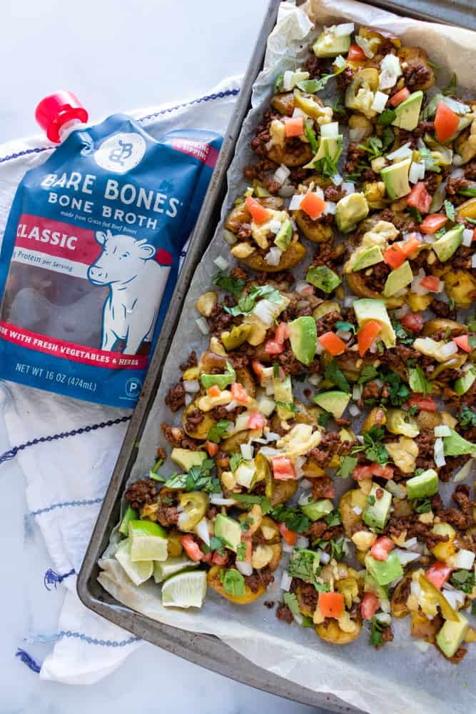 crispy smashed potato nachos on a tray next to a package of bare bones broth