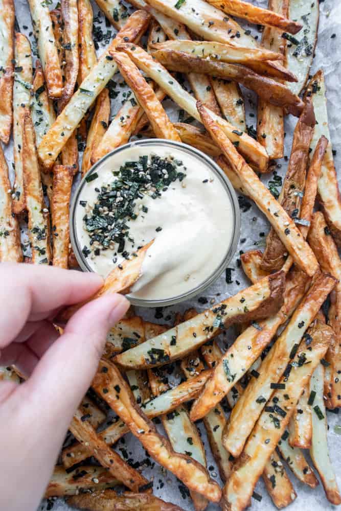 furikake french fries on a platter with a hand with one of the fries dipping it into the sauce