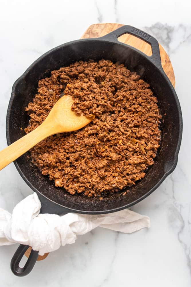 ground taco meat in a cast iron skillet with a wooden spoon in it