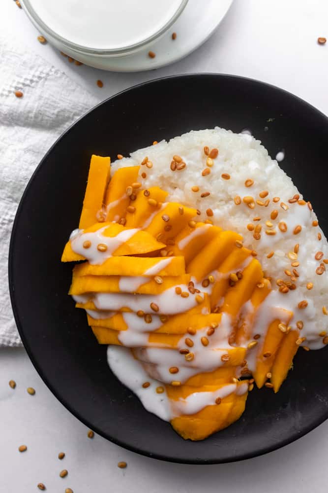 mango sticky rice on a plate next to the coconut cream