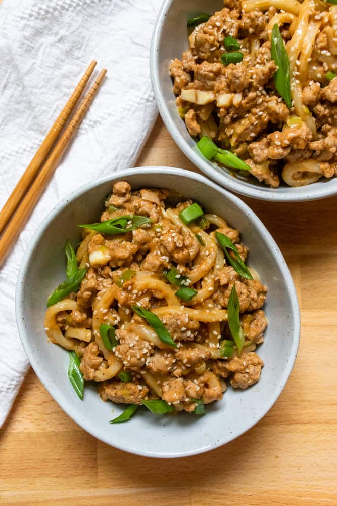two bowls of peanut garlic udon stir fry next to chopsticks