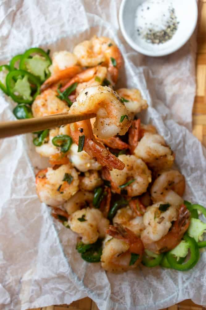 Salt & Pepper Shrimp in a basket and one is being held up by chopsticks for a closeup