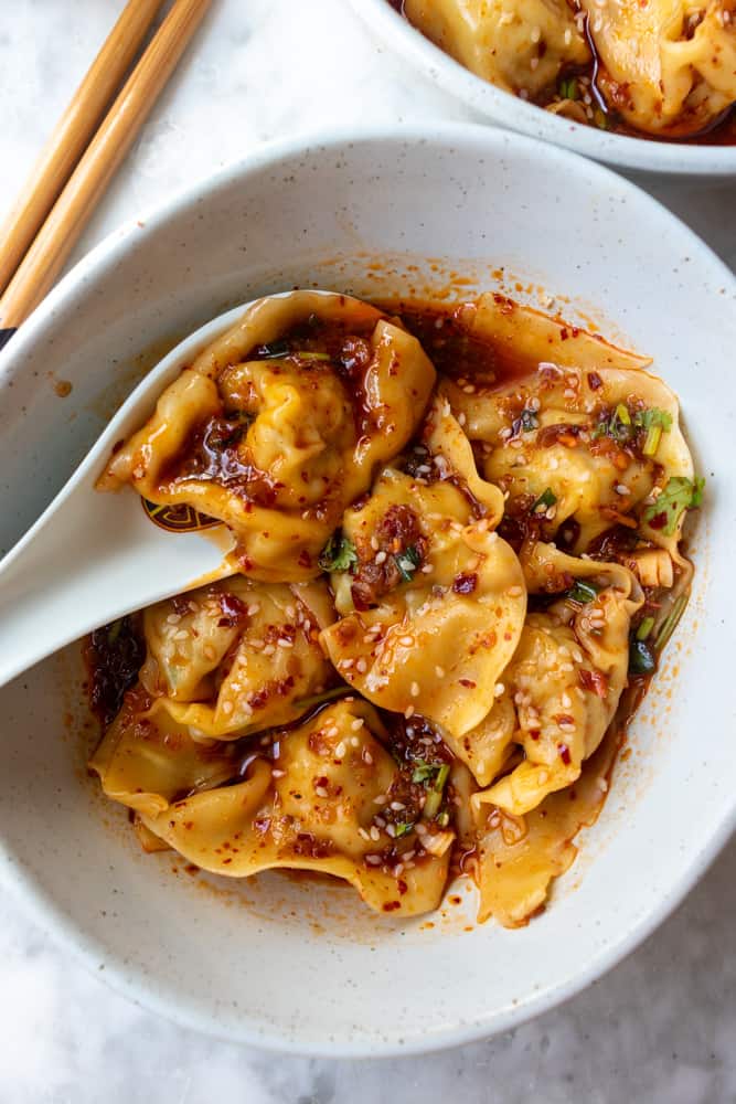 Spicy Szechuan Wontons in a bowl and one if being held in a soup spoon