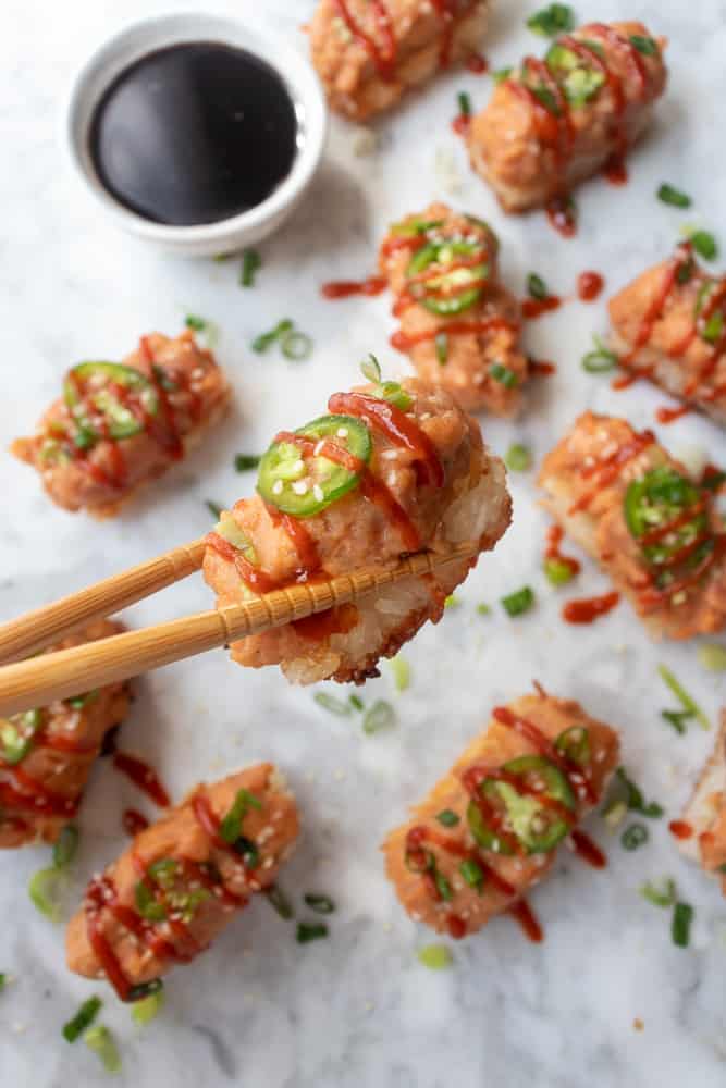 one Spicy Tuna Crispy Rice held up by a pair of chopsticks