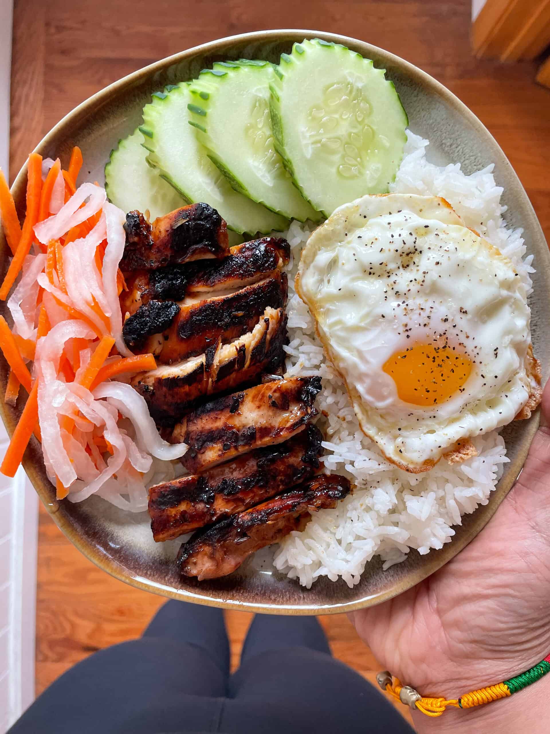 vietnamese lemongrass chicken served with rice, pickled veggies, cucumber slices, and a fried egg